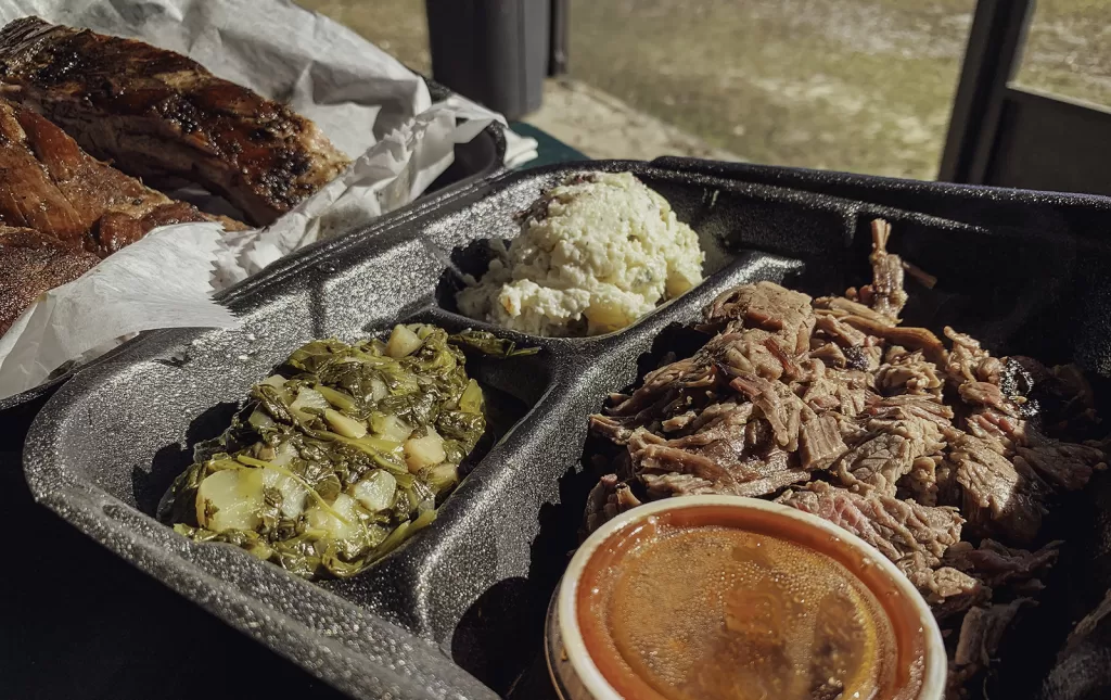 A plate of barbecue with brisket, ribs, greens and horseradish potato salad.