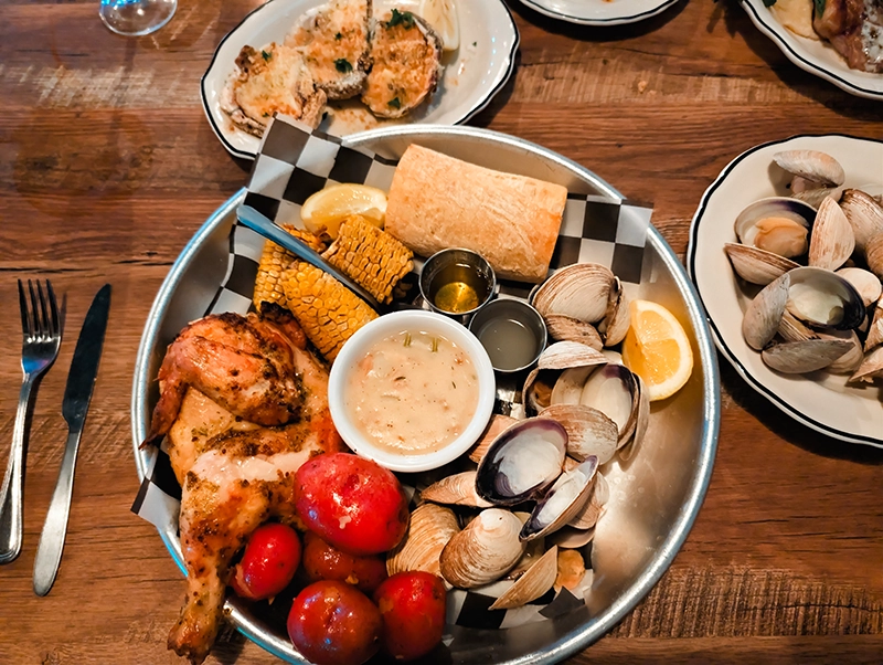 A plate with clam, potatoes, corn and chicken.